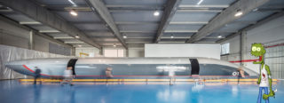 La cápsula de hyperloop Quintero One vista desde un lateral. Un simpático zombi de dibujos animados sonríe a la derecha.